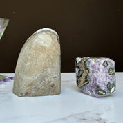 Two Uruguayan amethyst clusters with agate, one tall gray geode and one vibrant purple cube.