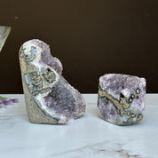 Two vibrant purple amethyst geode clusters with agate formations on a white marble surface.