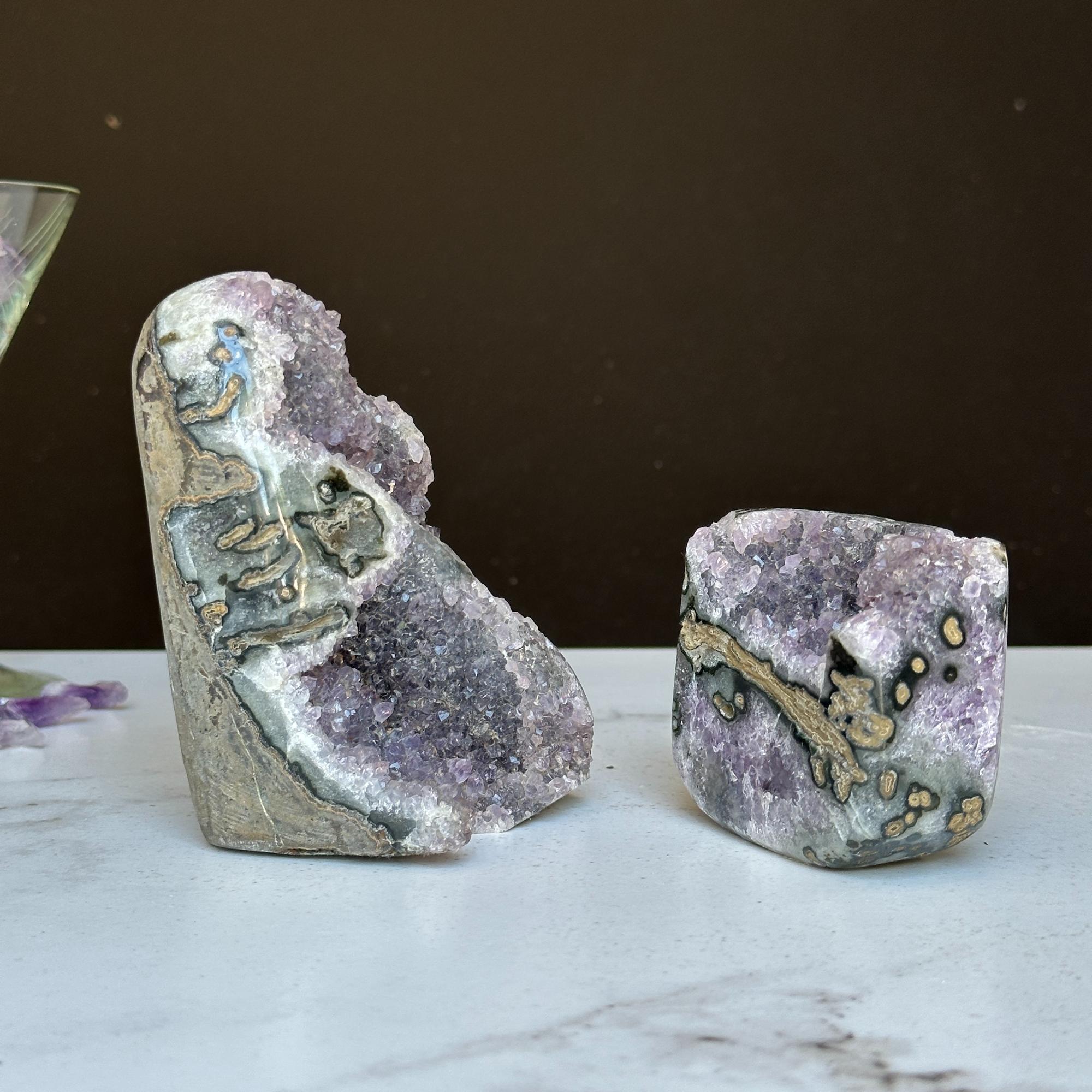 Two vibrant purple amethyst geode clusters with agate formations on a white marble surface.