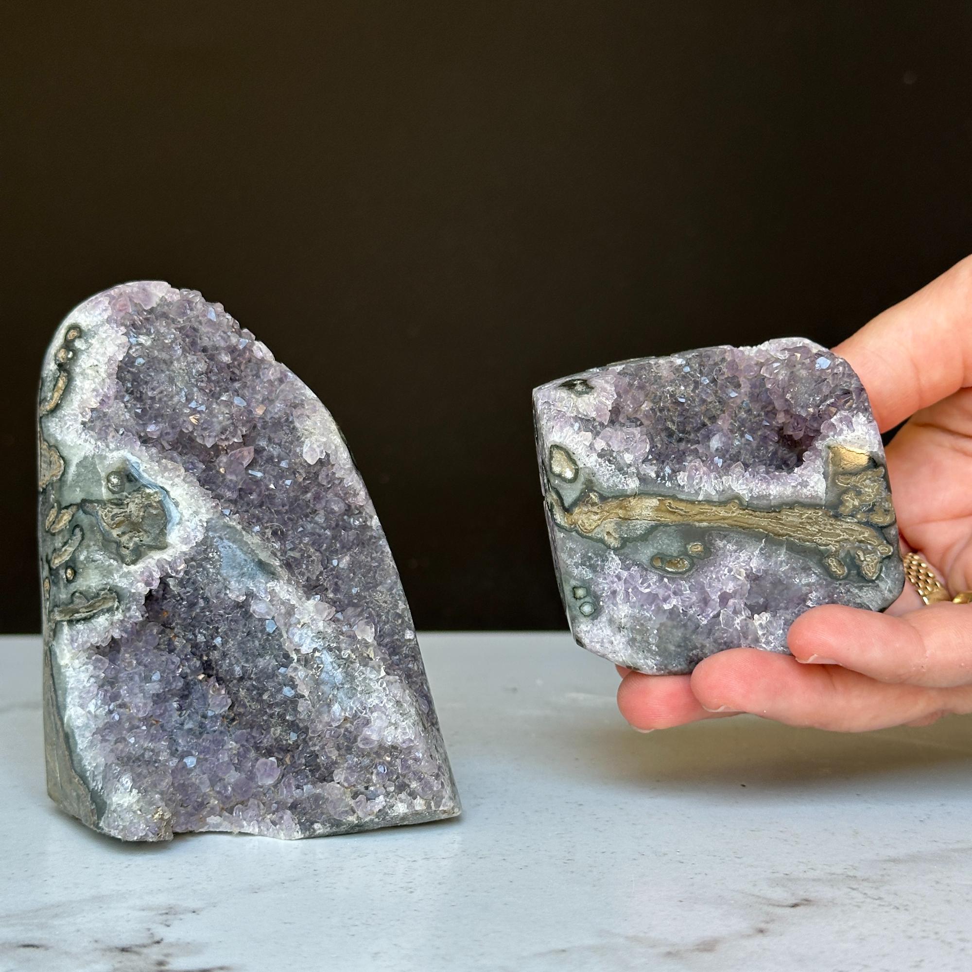 Two vibrant purple amethyst geode clusters with gray agate, one held in a hand.
