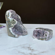 Two vibrant purple amethyst clusters with agate formations, one large upright and one small rectangular.