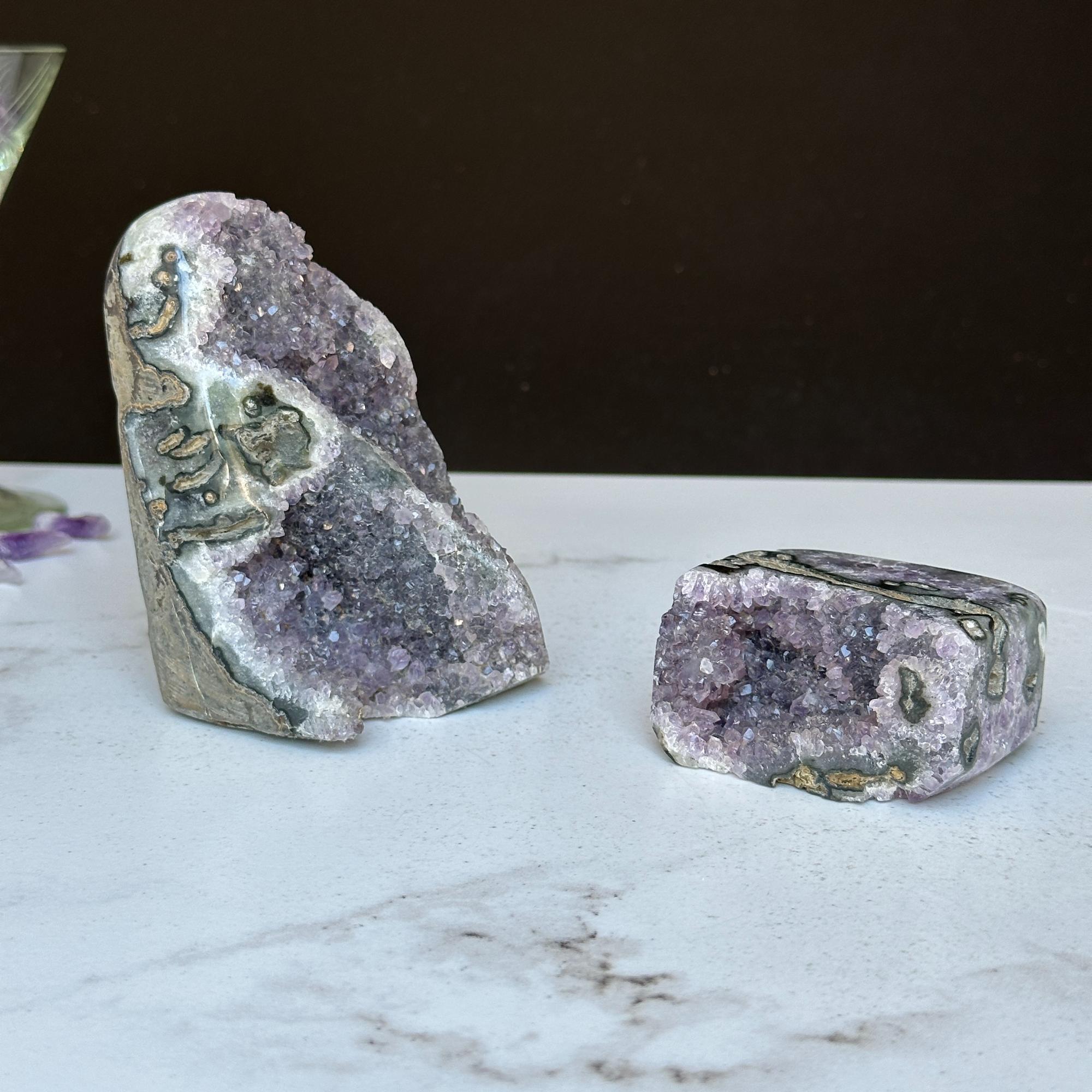 Two vibrant purple amethyst clusters with agate formations, one large upright and one small rectangular.
