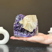 Hand holding a vibrant deep purple amethyst geode cluster with a large light yellow crystal. Stunning natural decor.