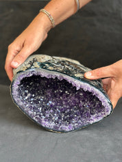 Person holding a large amethyst geode against a dark background