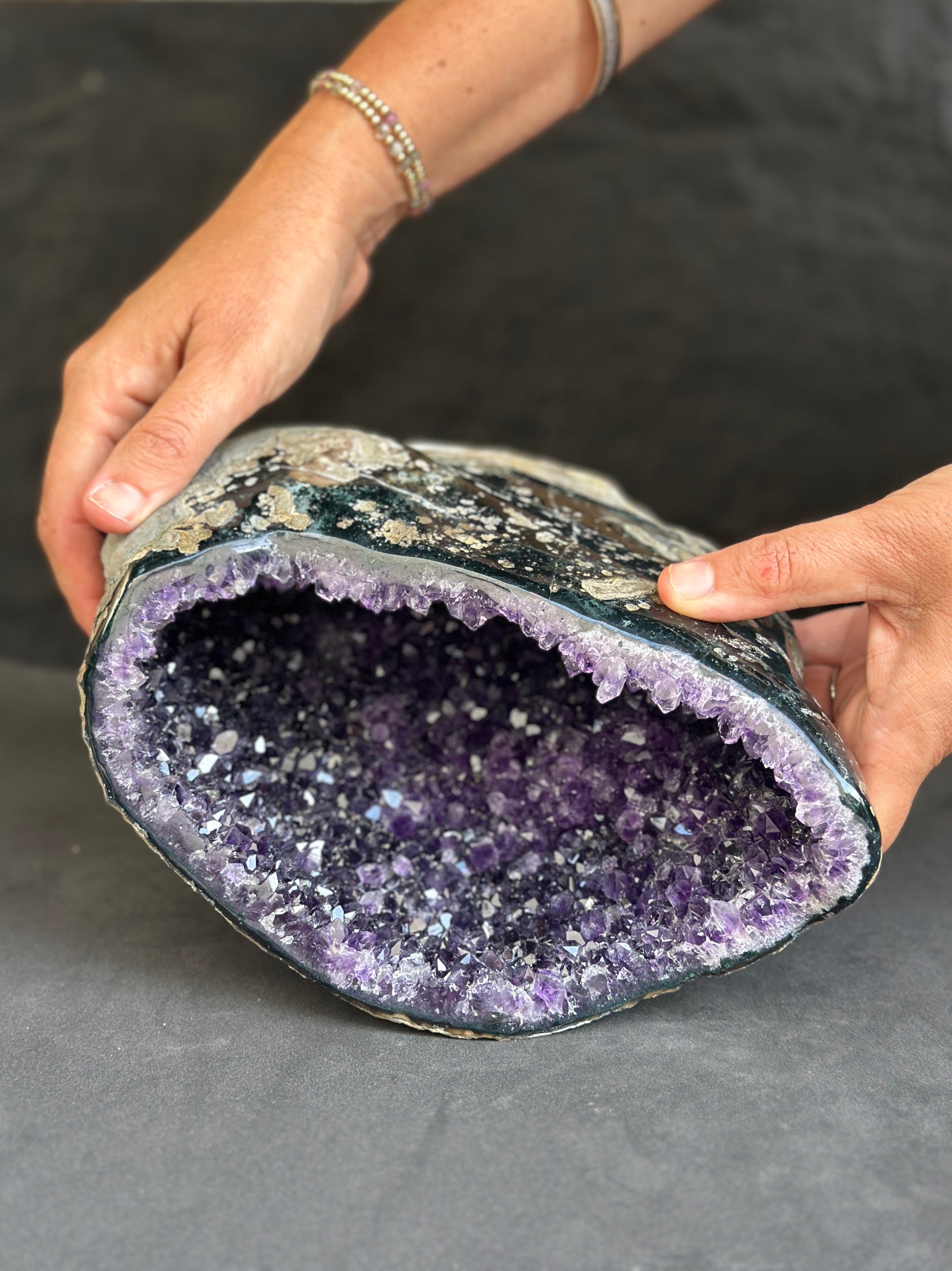Person holding a large amethyst geode against a dark background