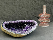 Amethyst geode crystal bowl and pink glass candle holder on a dark surface
