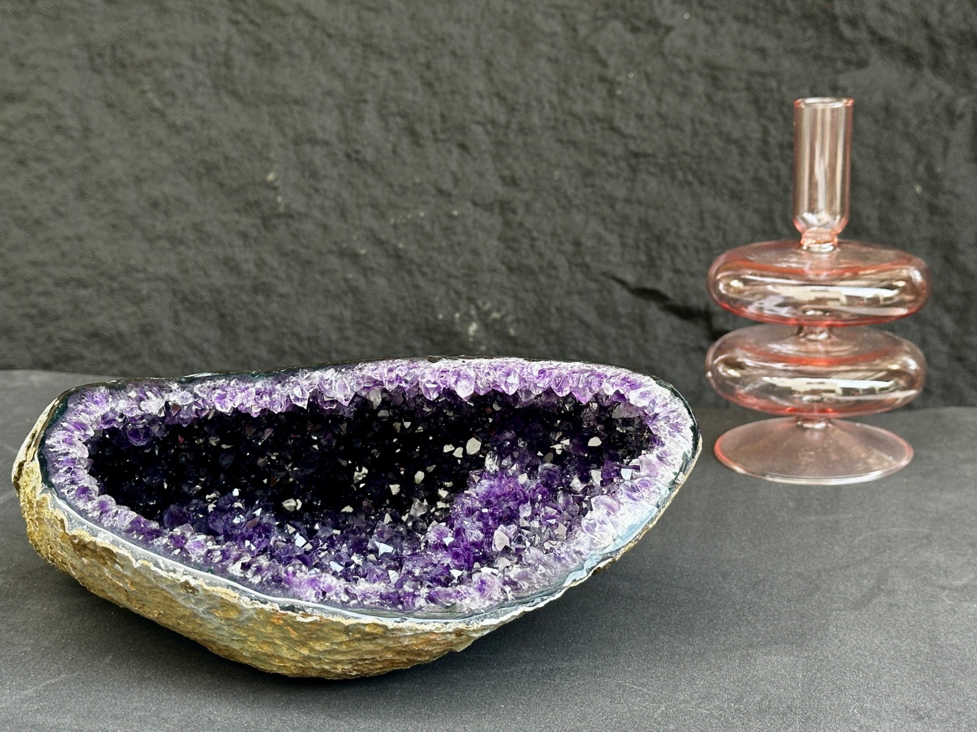 Amethyst geode crystal bowl and pink glass candle holder on a dark surface