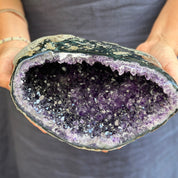 Person holding a large amethyst geode with visible purple crystals.