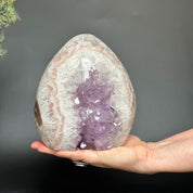 Hand holding a 7-inch Uruguayan amethyst and agate geode cave with vibrant purple crystals.