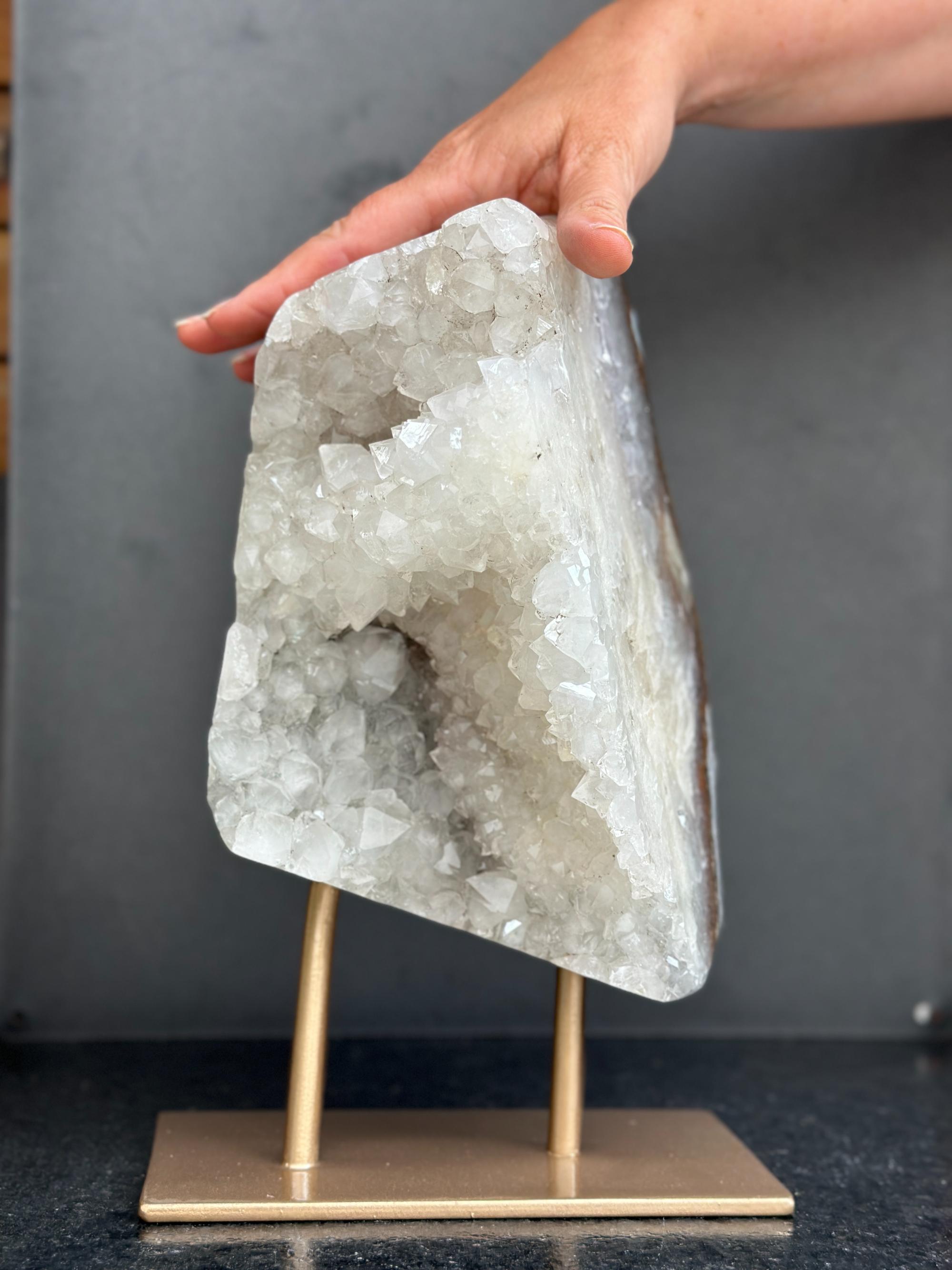 Geode crystal on a stand with a hand holding it against a gray background