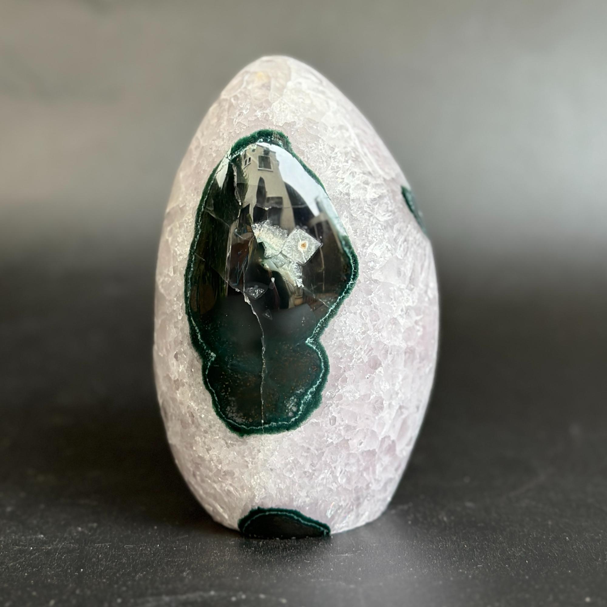 A polished crystal stone featuring a light pinkish-white textured exterior with prominent dark green and black agate inclusions, standing upright on a dark surface.
