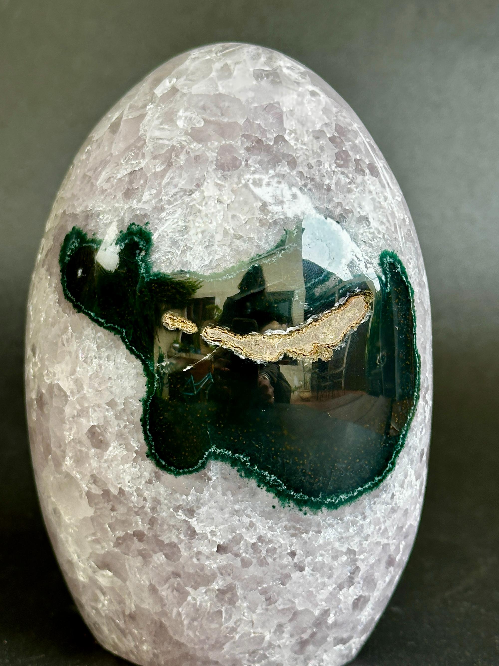 A polished oval stone featuring a light lavender-gray crystalline body with a prominent dark green agate inlay and a thin gold edge, photographed on a dark gray background.