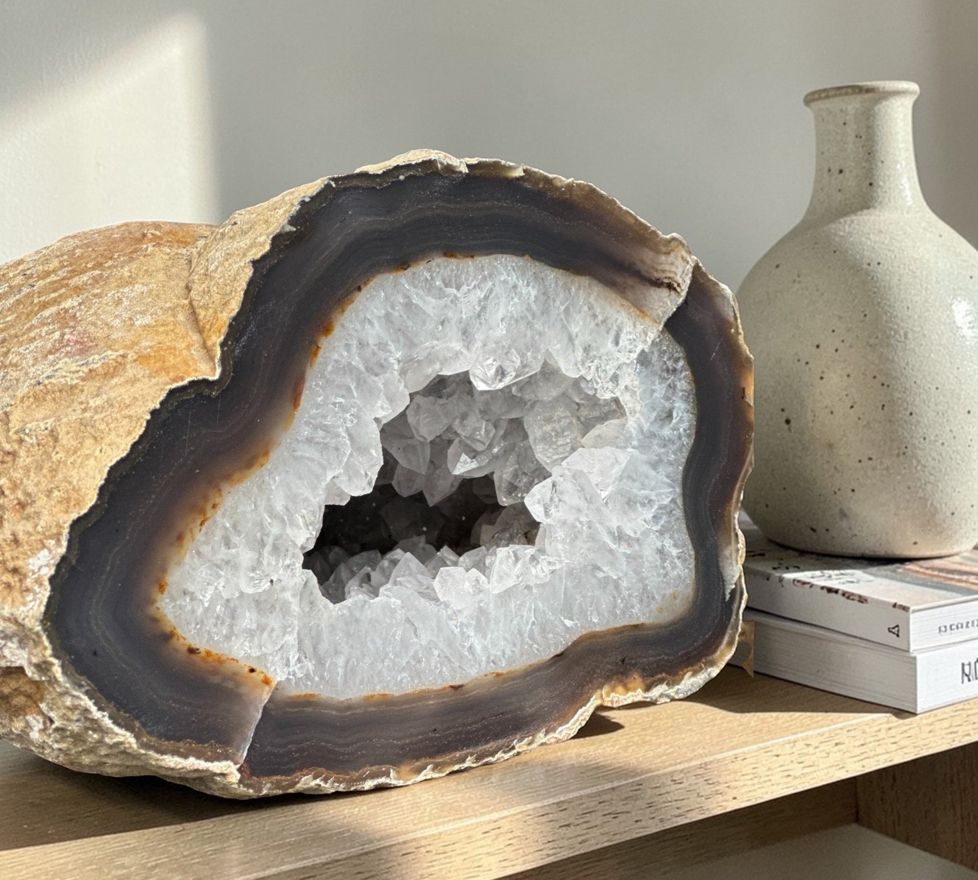 Large white quartz crystal geode cave with sparkling clear druzy crystals, brown rock exterior, and dark banded layers.
