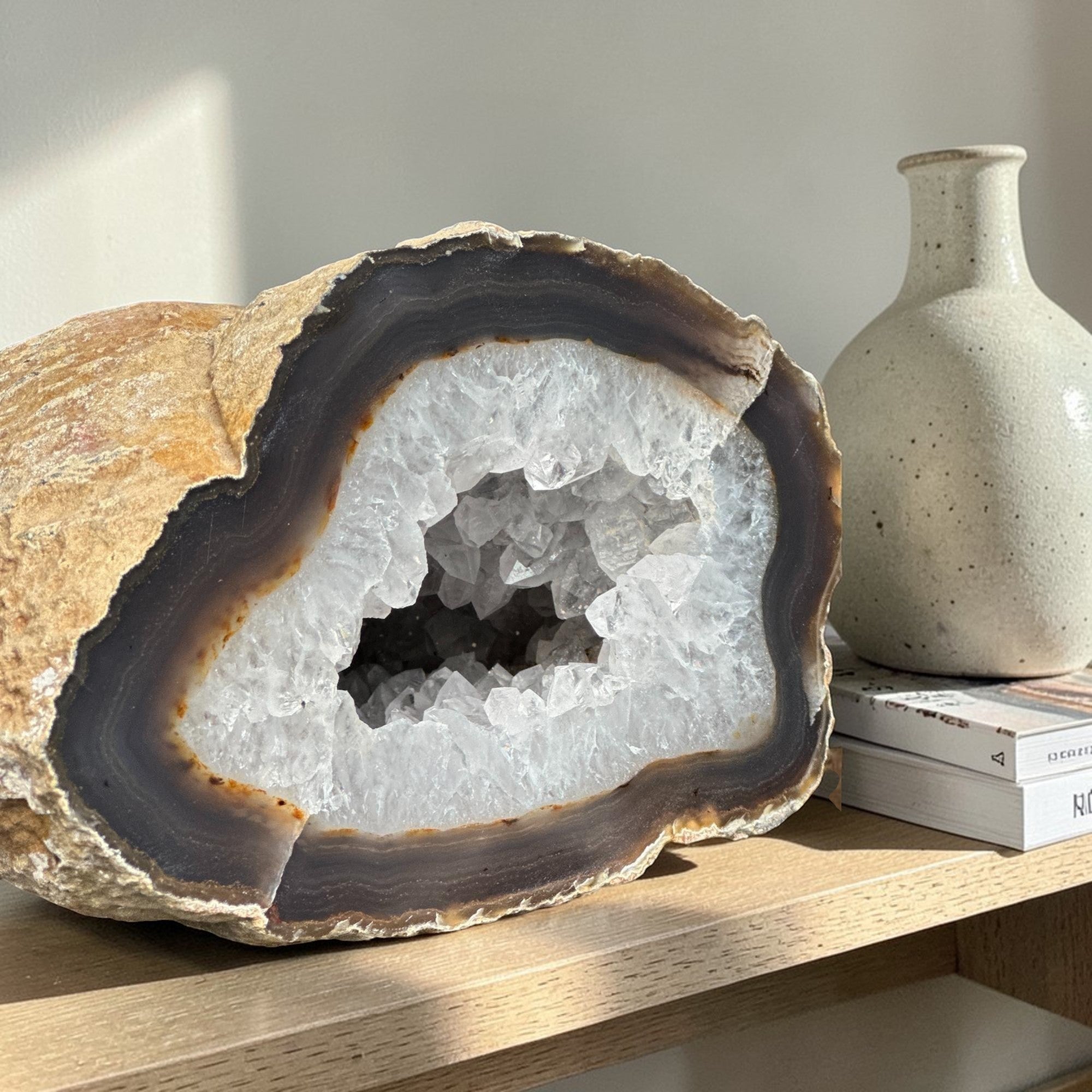 Large white quartz crystal geode cave with sparkling clear druzy crystals, brown rock exterior, and dark banded layers.