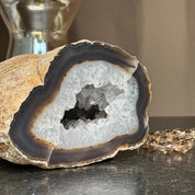 Extra large white quartz druzy geode cave with dark banded layers and natural brown rock exterior.