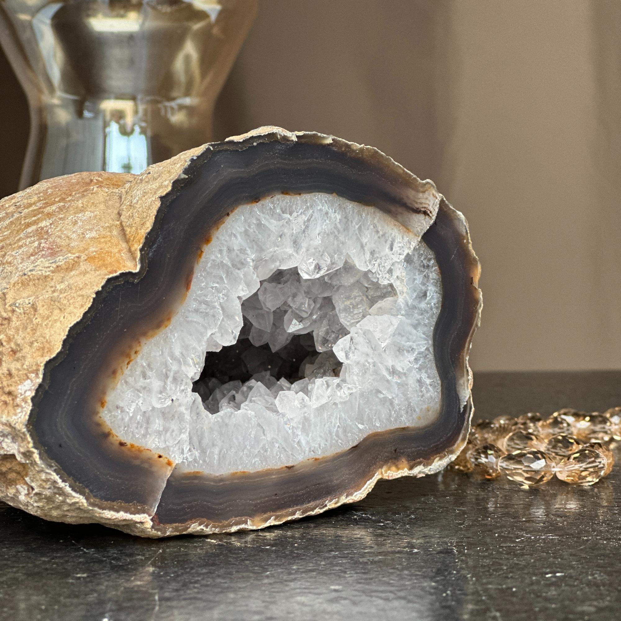 Extra large white quartz druzy geode cave with dark banded layers and natural brown rock exterior.