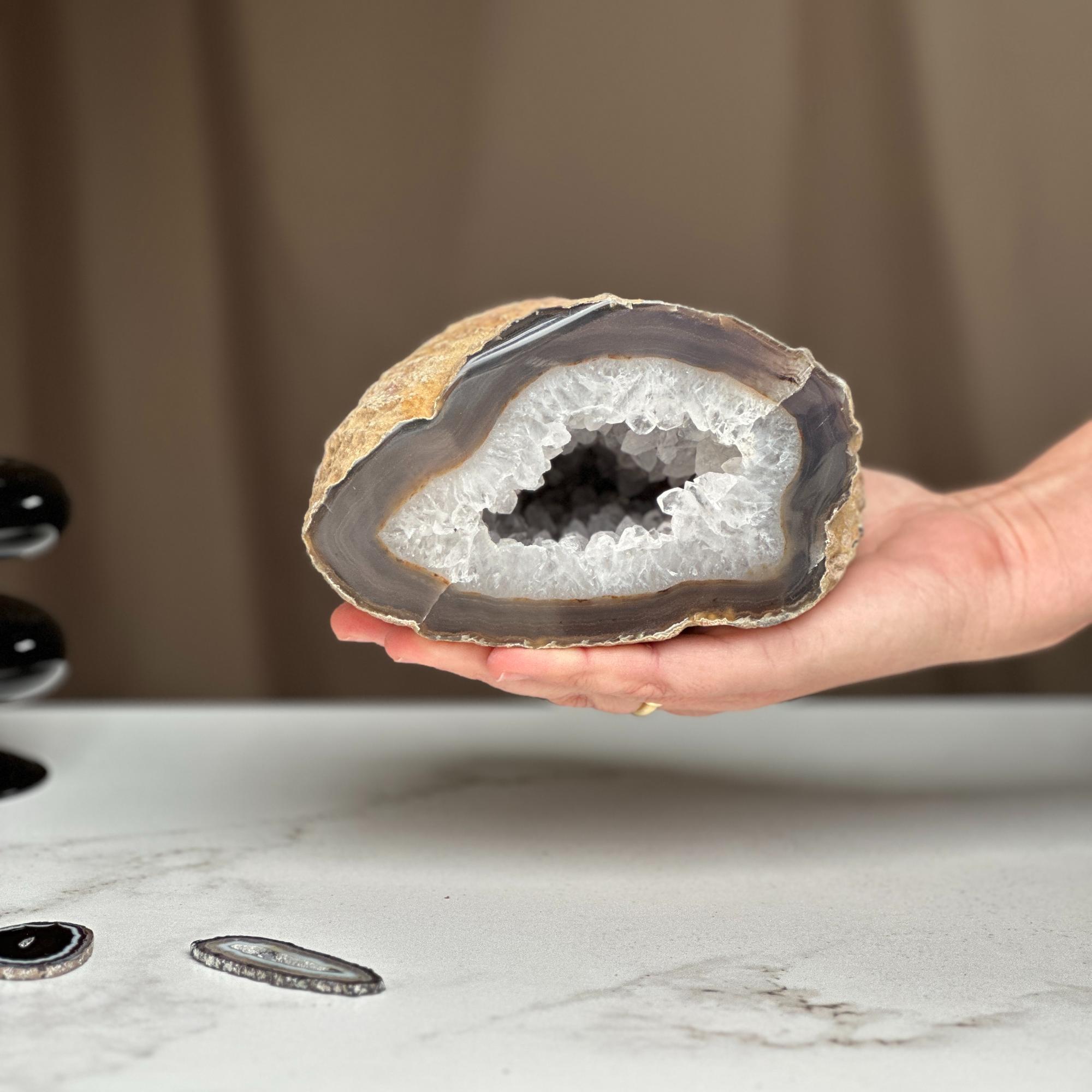 Hand holding a large white quartz crystal geode cave, revealing sparkling druzy interior and brown layered semi-precious stone.