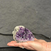 Hand holding a purple crystal cluster against a dark gray background