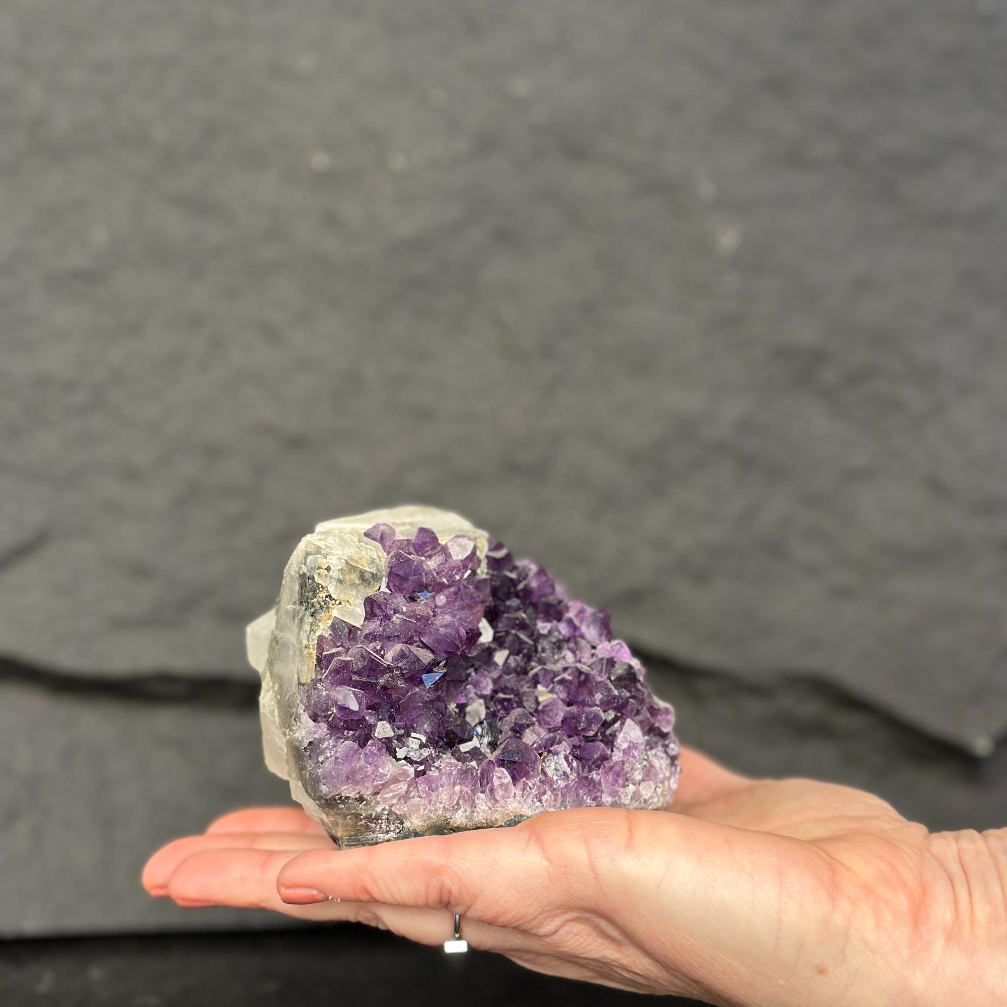 Hand holding a purple crystal cluster against a dark gray background
