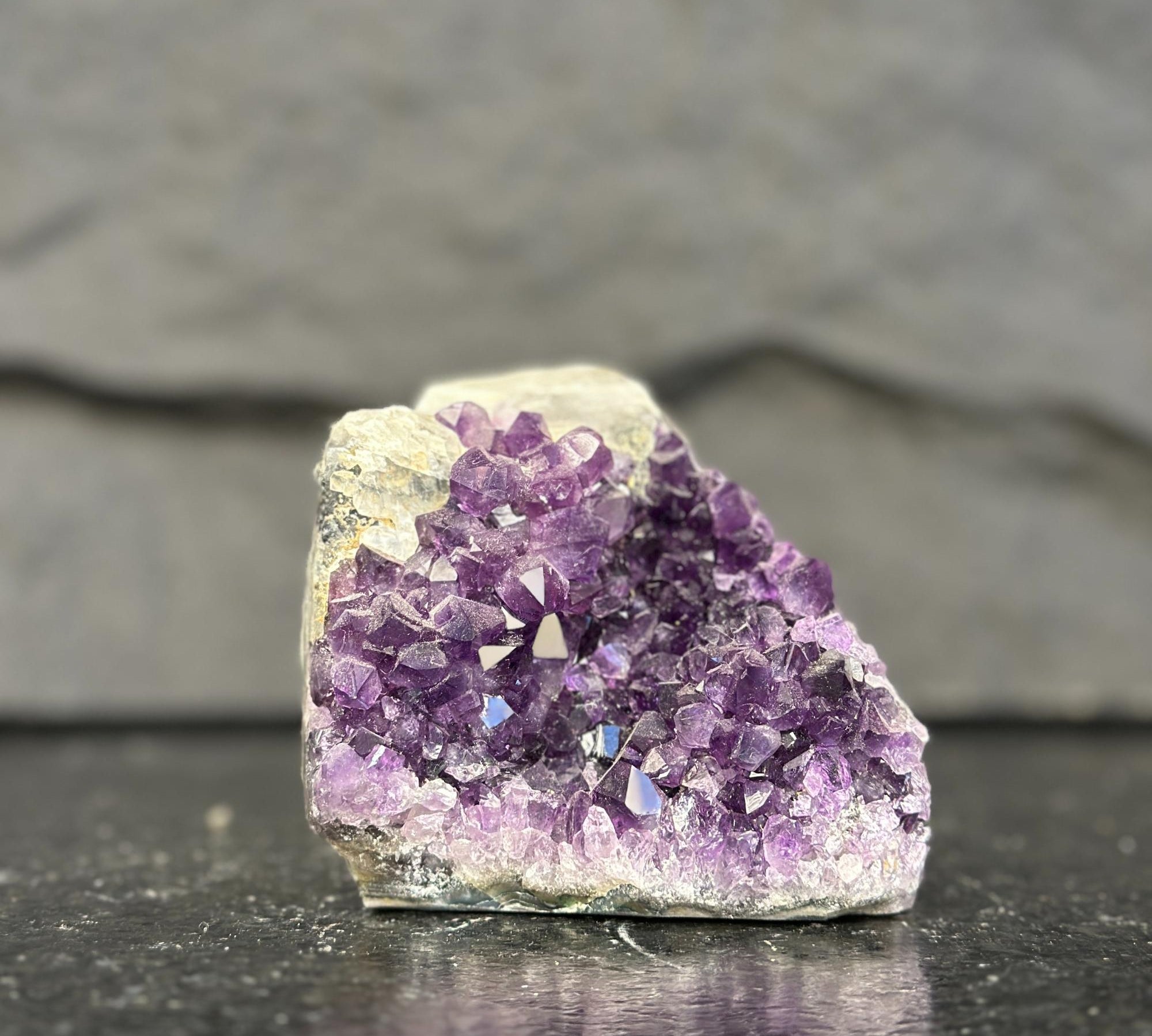 Amethyst crystal cluster on a dark surface with a gray background