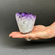 Hand holding a crystal with purple top and white base against a dark background