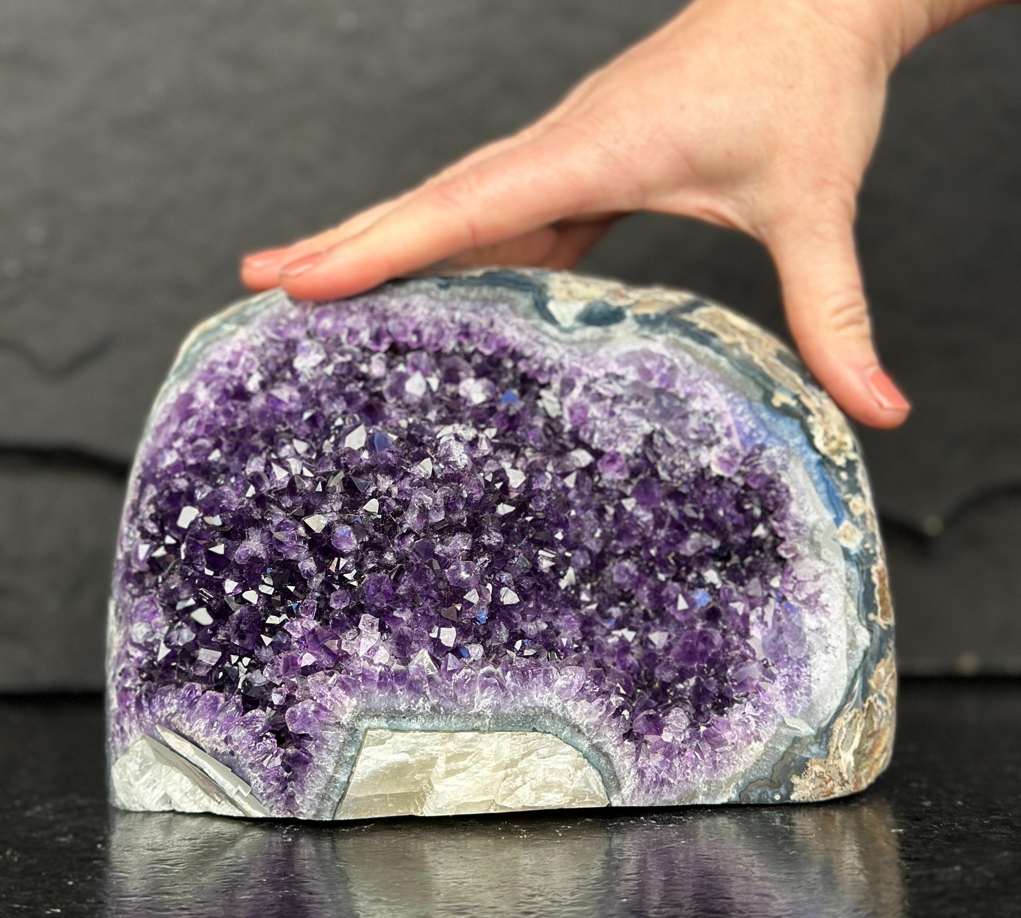 Amethyst crystal geode with a hand touching it on a dark surface