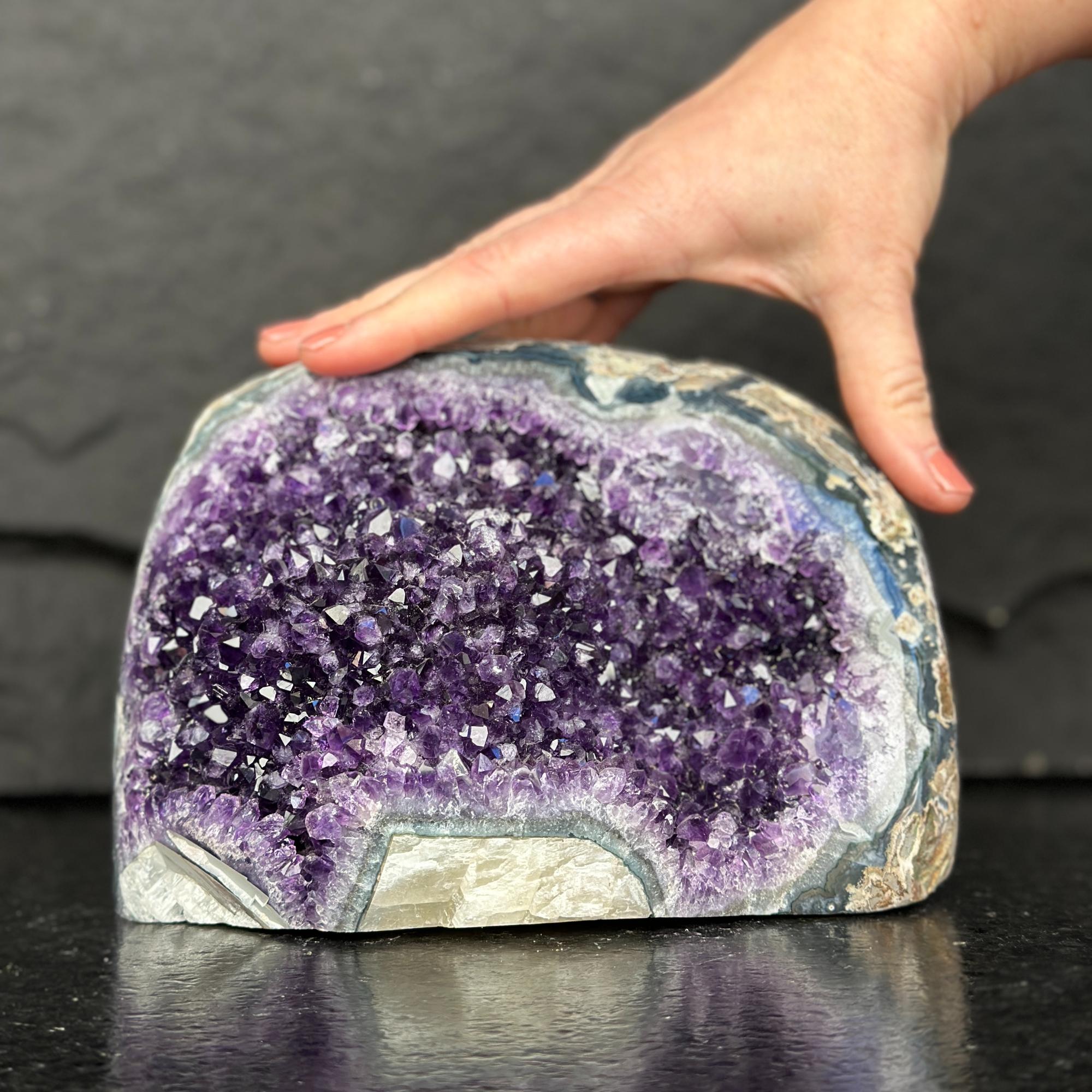 Amethyst crystal geode with a hand touching it on a dark surface