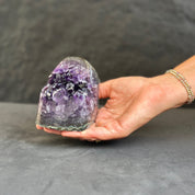 Hand holding a large amethyst crystal against a dark background