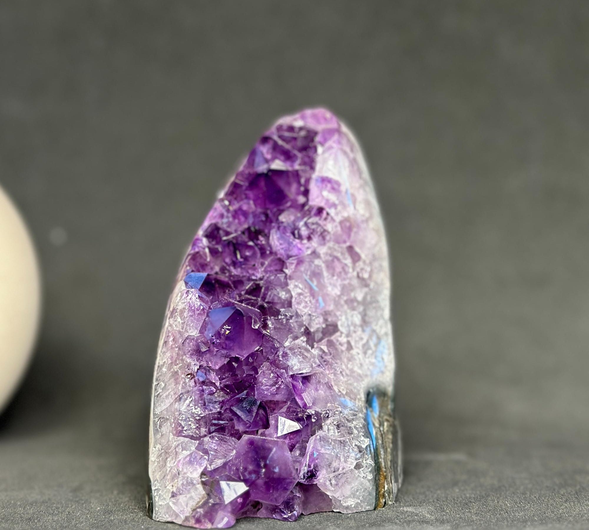 A natural amethyst crystal cluster geode specimen with deep purple and lavender crystals transitioning to clear white quartz points, displayed on a neutral gray background.