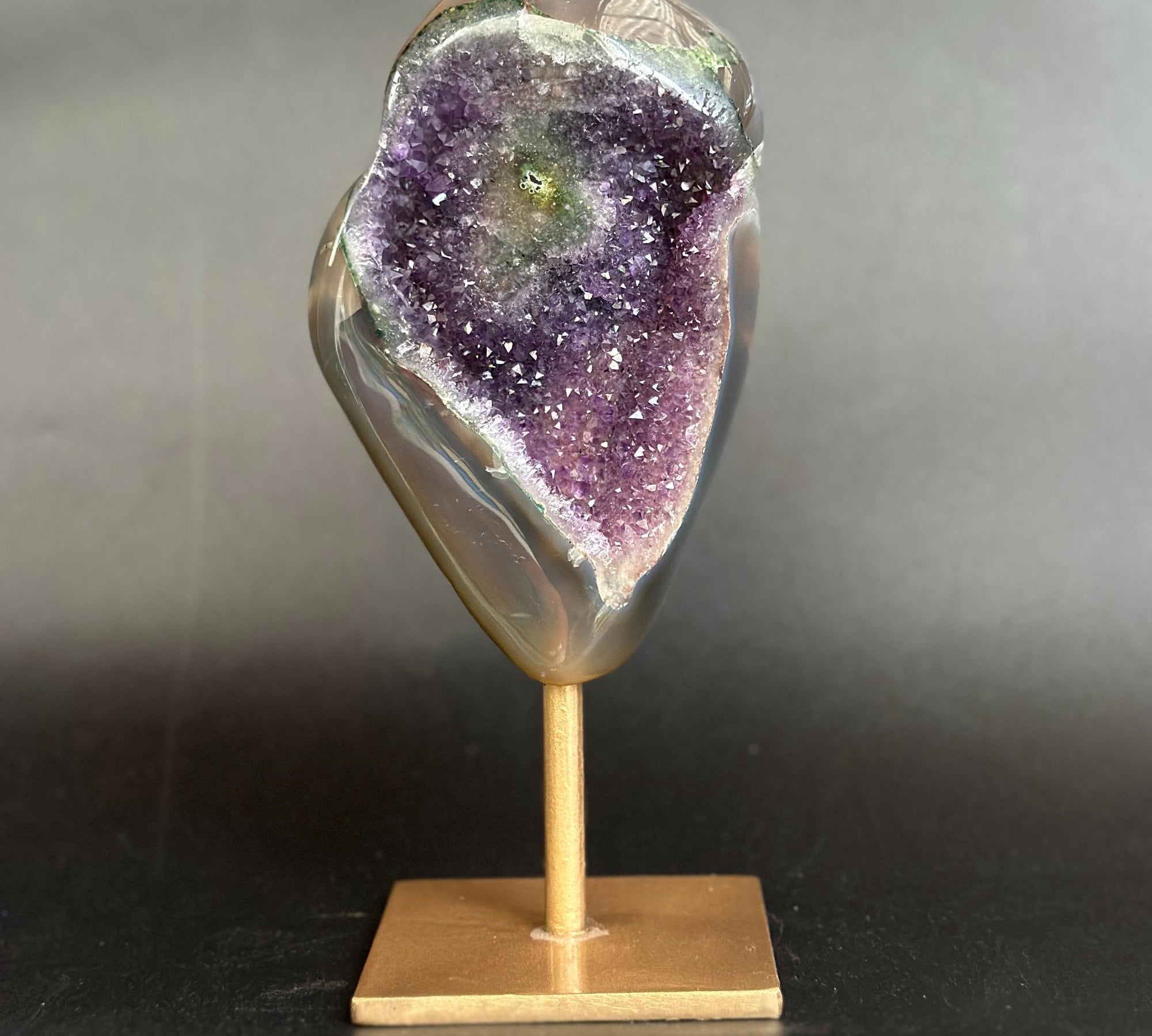 A polished geode specimen with a purple amethyst-like interior and a smooth gray outer rind, mounted on a small wooden display stand against a dark gray background.