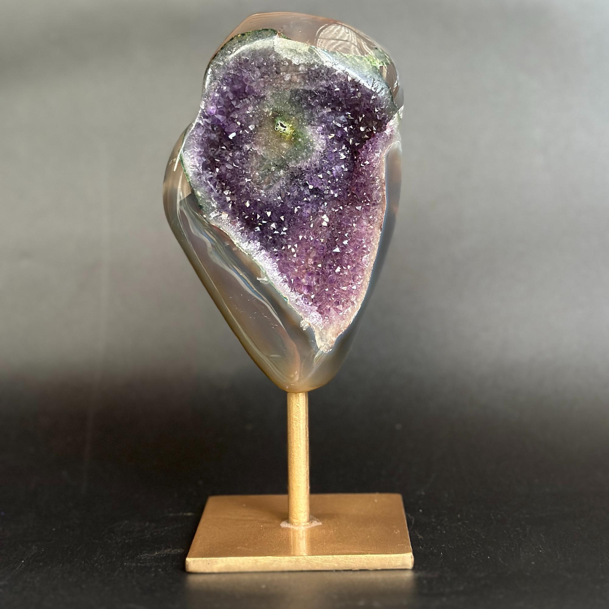 A polished geode specimen with a purple amethyst-like interior and a smooth gray outer rind, mounted on a small wooden display stand against a dark gray background.