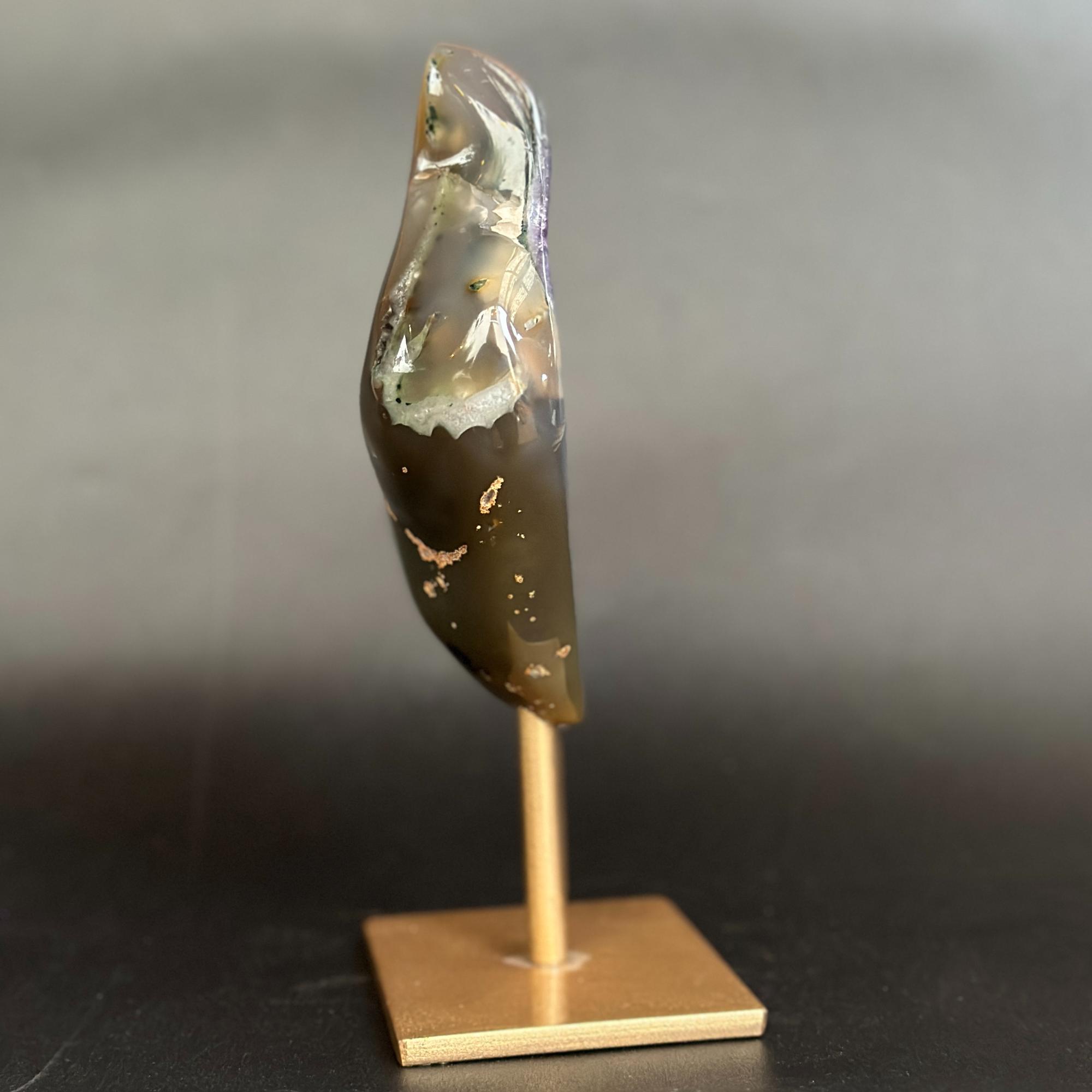 An amethyst and agate geode specimen on a wooden display stand, featuring a purple amethyst crystal cavity and green banded edges, set against a dark gray background.