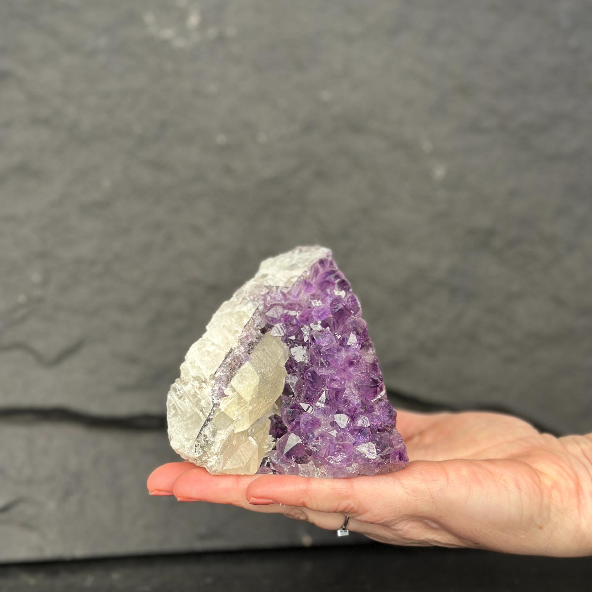 Hand holding a large amethyst crystal against a dark gray background