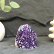 Purple crystal rock on a dark surface with blurred greenery and white object in the background