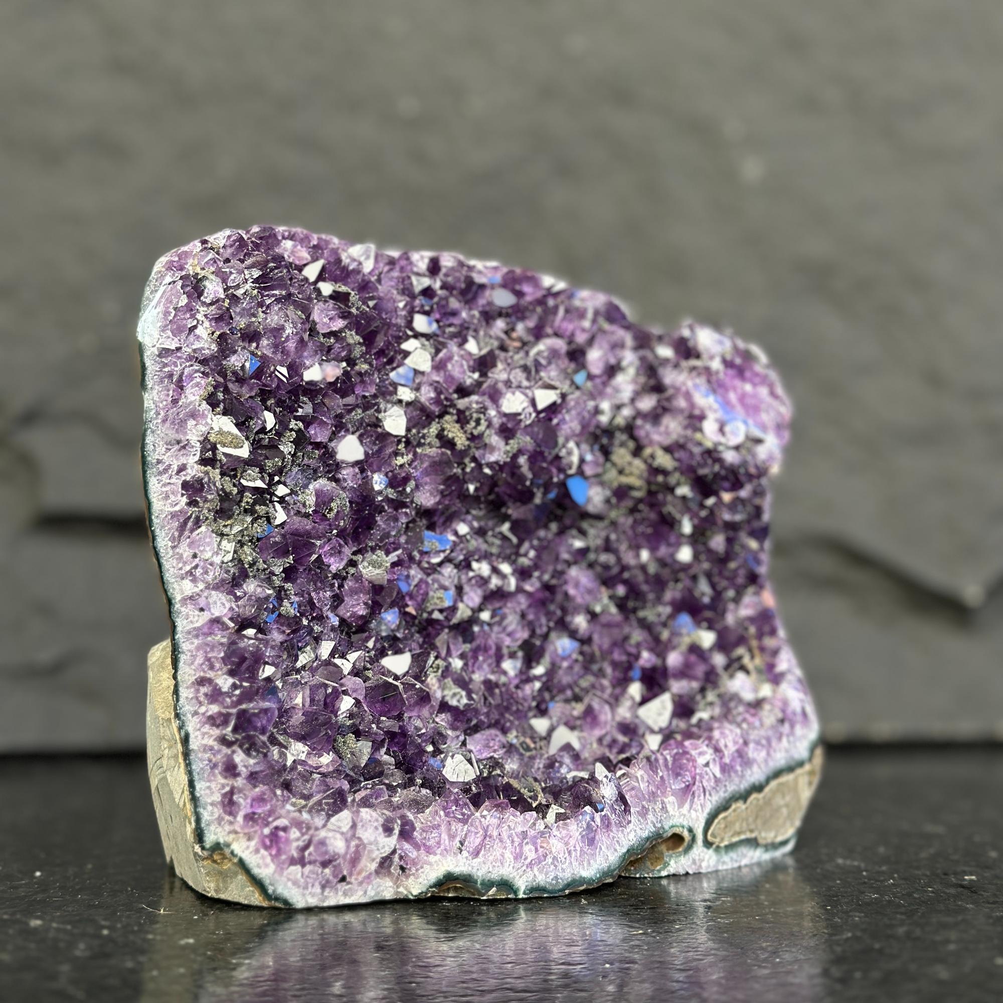 Amethyst crystal cluster on a dark surface with a gray background