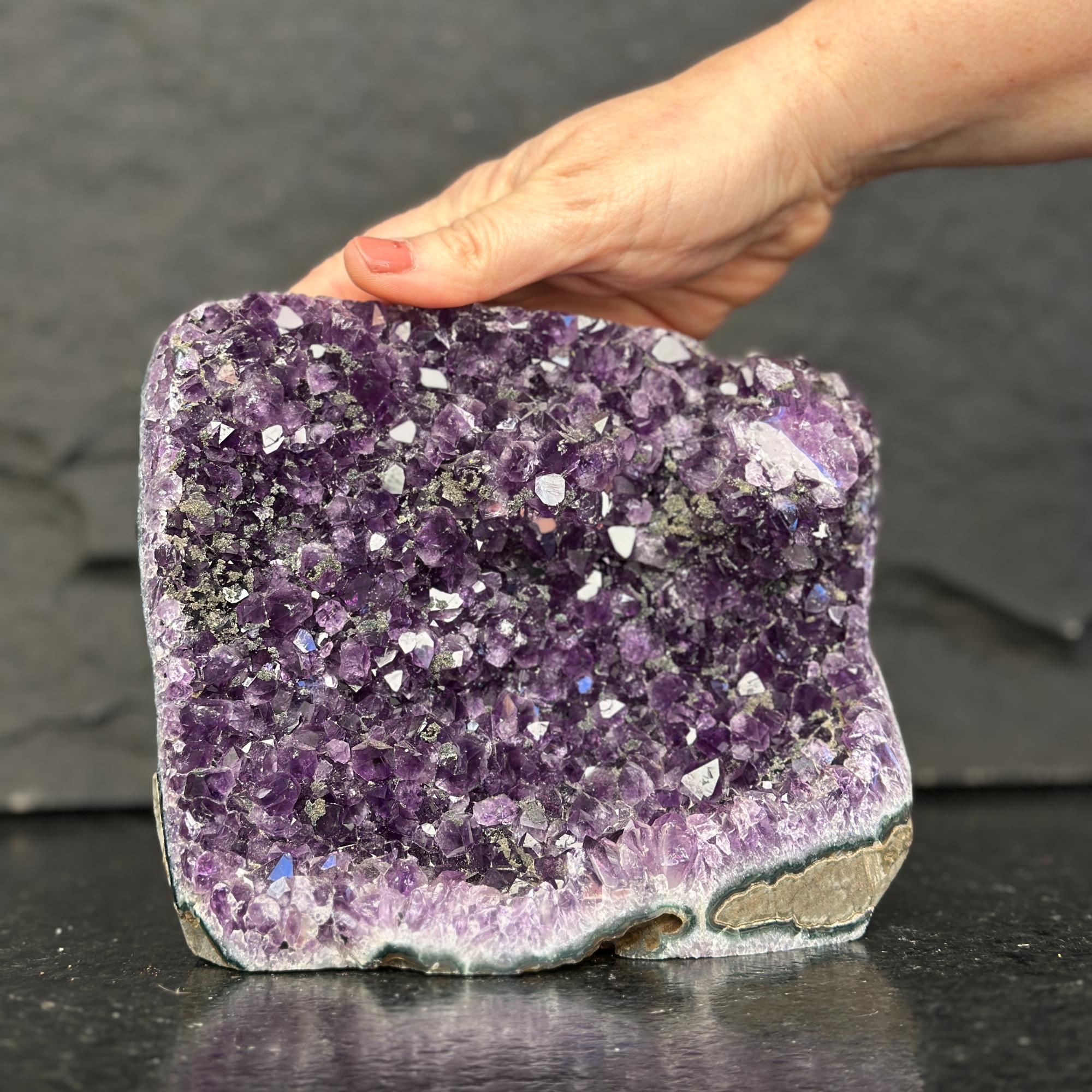 Amethyst crystal block held by a hand against a dark background