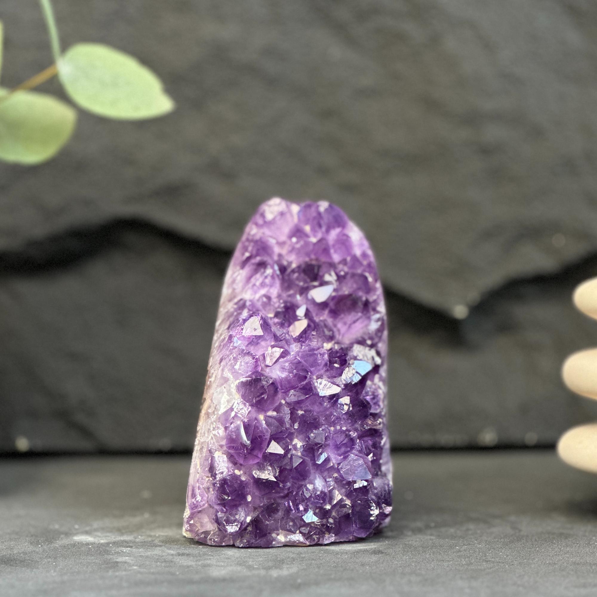 A natural purple amethyst crystal cluster stone with sharp, faceted crystal points, standing upright on a dark slate surface against a dark gray slate background.