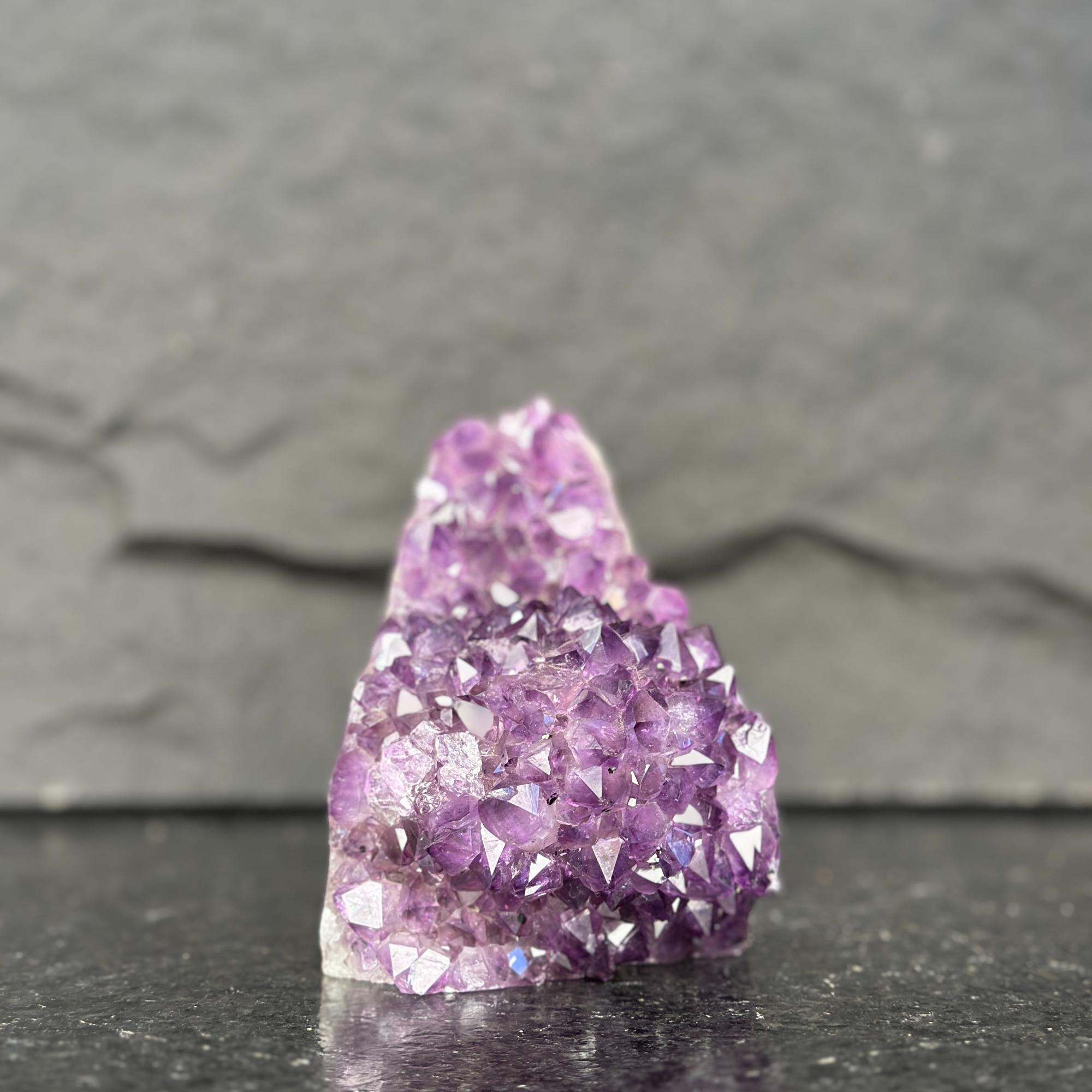 Purple crystal cluster on a dark surface with a gray background