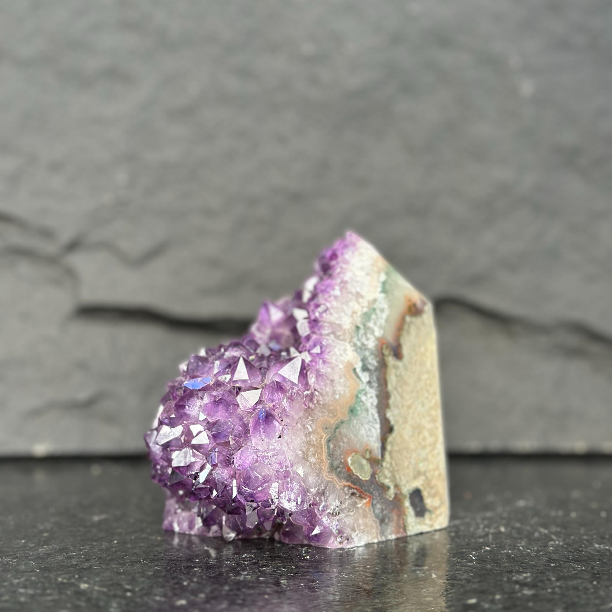 Amethyst crystal on a dark surface with a gray background