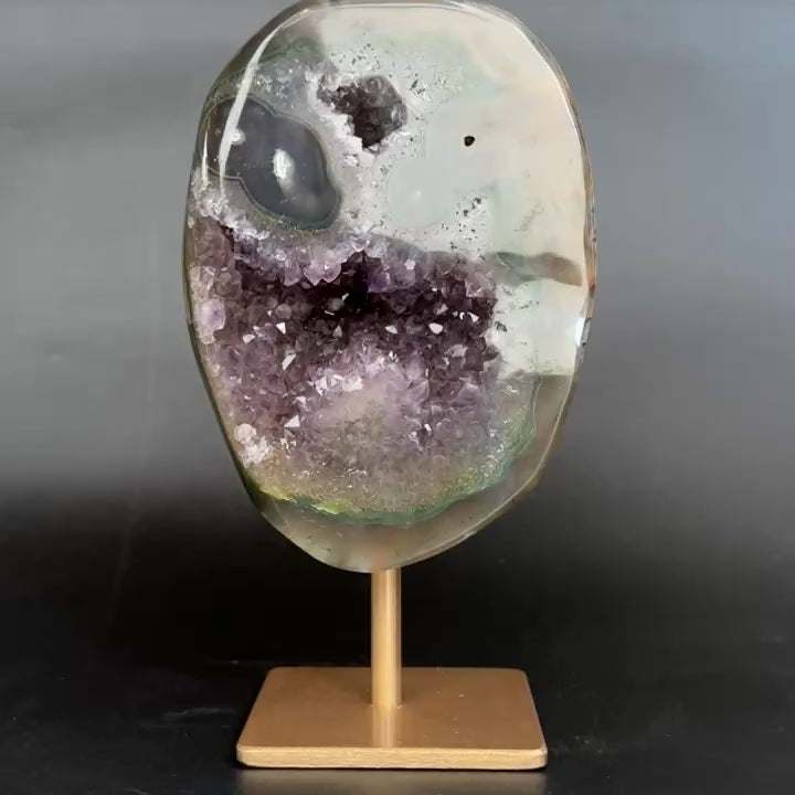 An amethyst and agate geode specimen on a wooden display stand, featuring a purple amethyst crystal cavity and green banded edges, set against a dark gray background.
