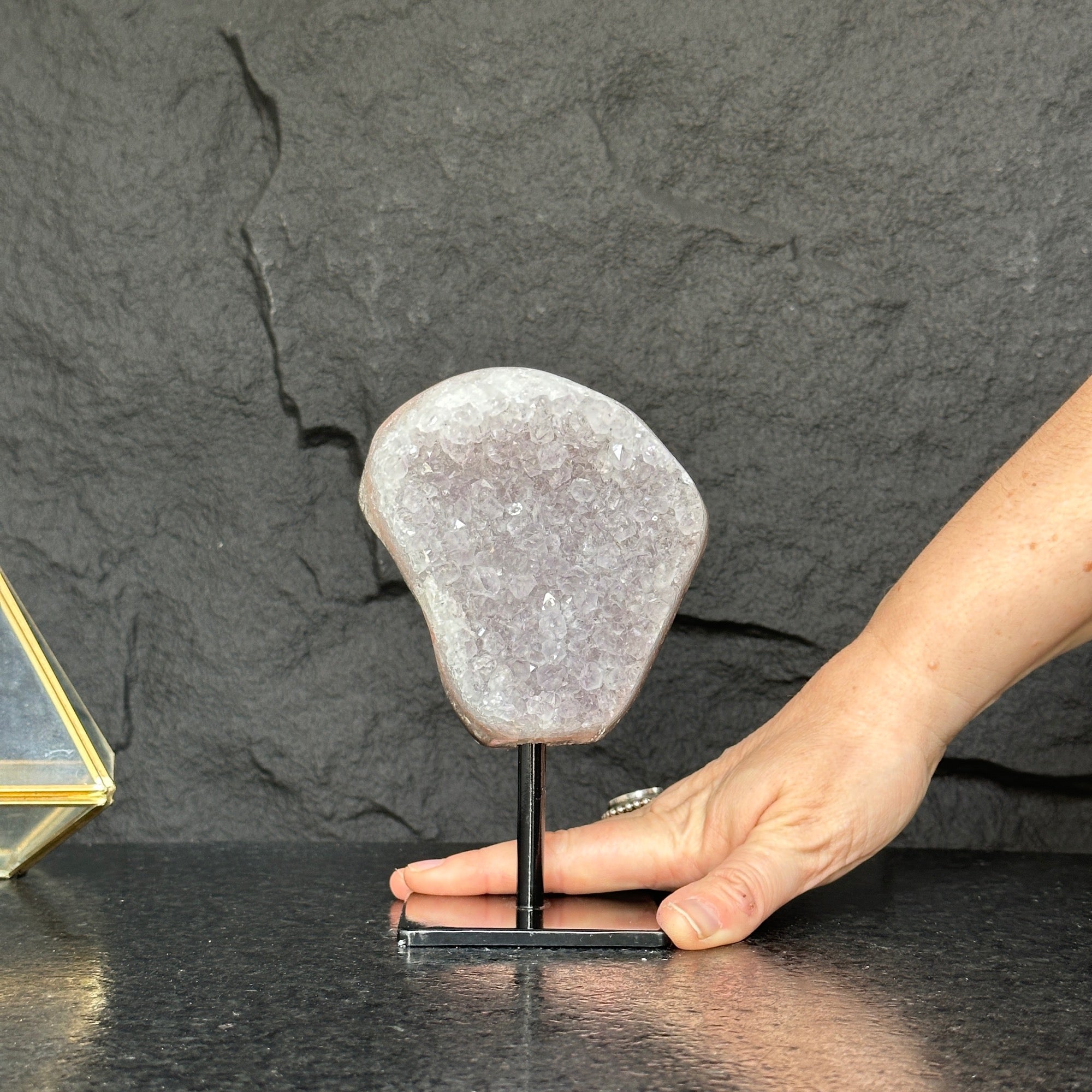 Hand holding a crystal on a stand against a dark stone background