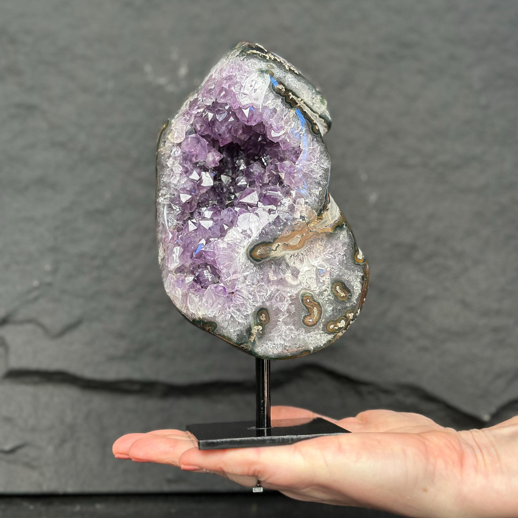 Amethyst geode on a stand held by a hand against a dark background