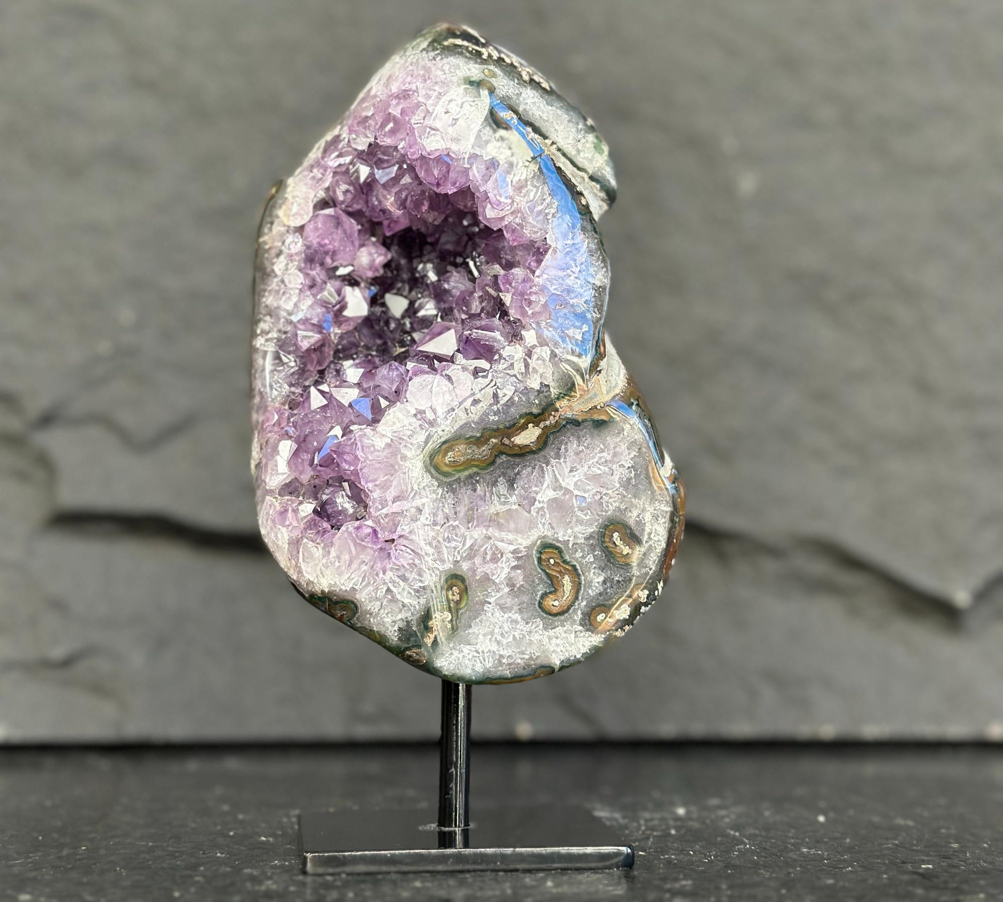 Geode with purple crystal on a stand against a gray background