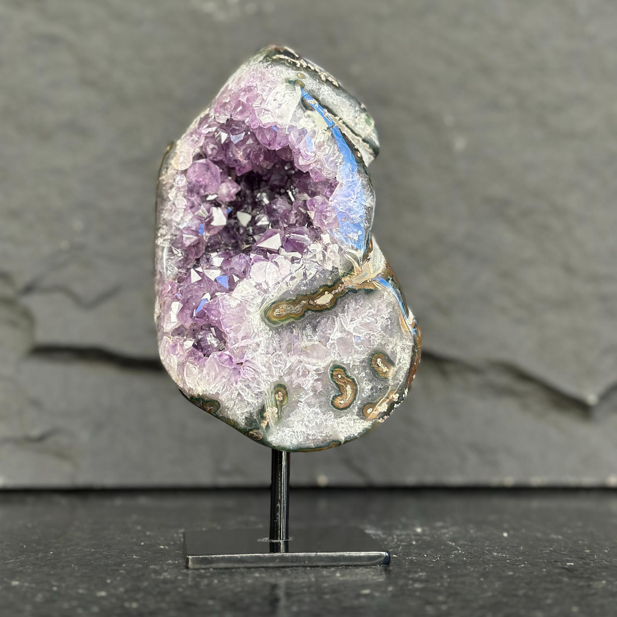 Geode with purple crystal on a stand against a gray background