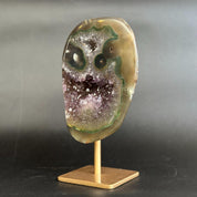 An amethyst and agate geode specimen on a wooden display stand, featuring a purple amethyst crystal cavity and green banded edges, set against a dark gray background.