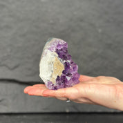 Hand holding a large amethyst crystal against a dark background