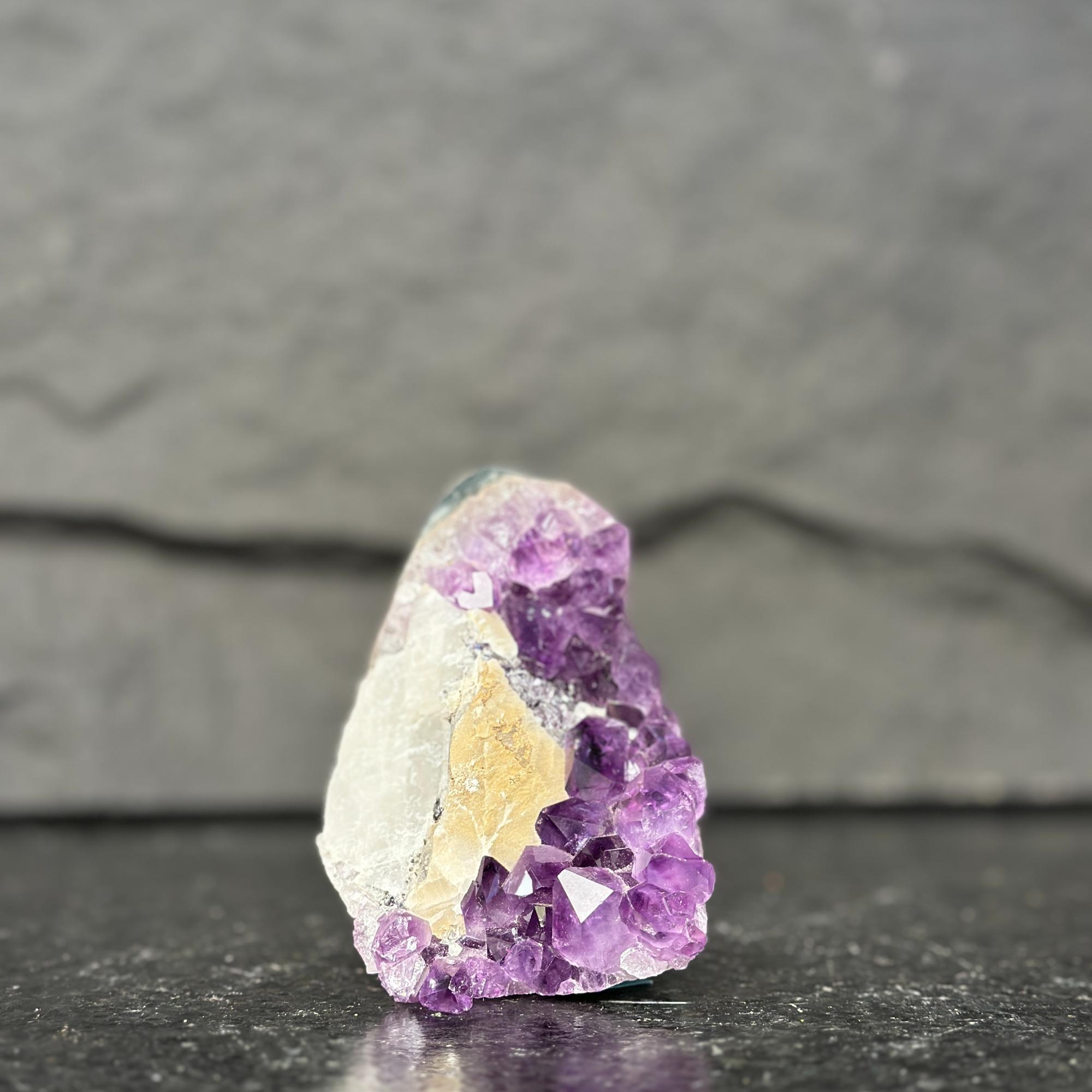 Amethyst crystal on a dark surface with a gray background