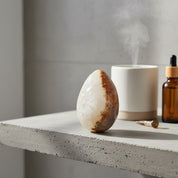 Aromatherapy diffuser, stone, and essential oil bottle on a concrete surface with a light background.