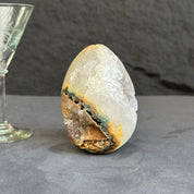 Geode crystal next to a glass goblet on a dark surface