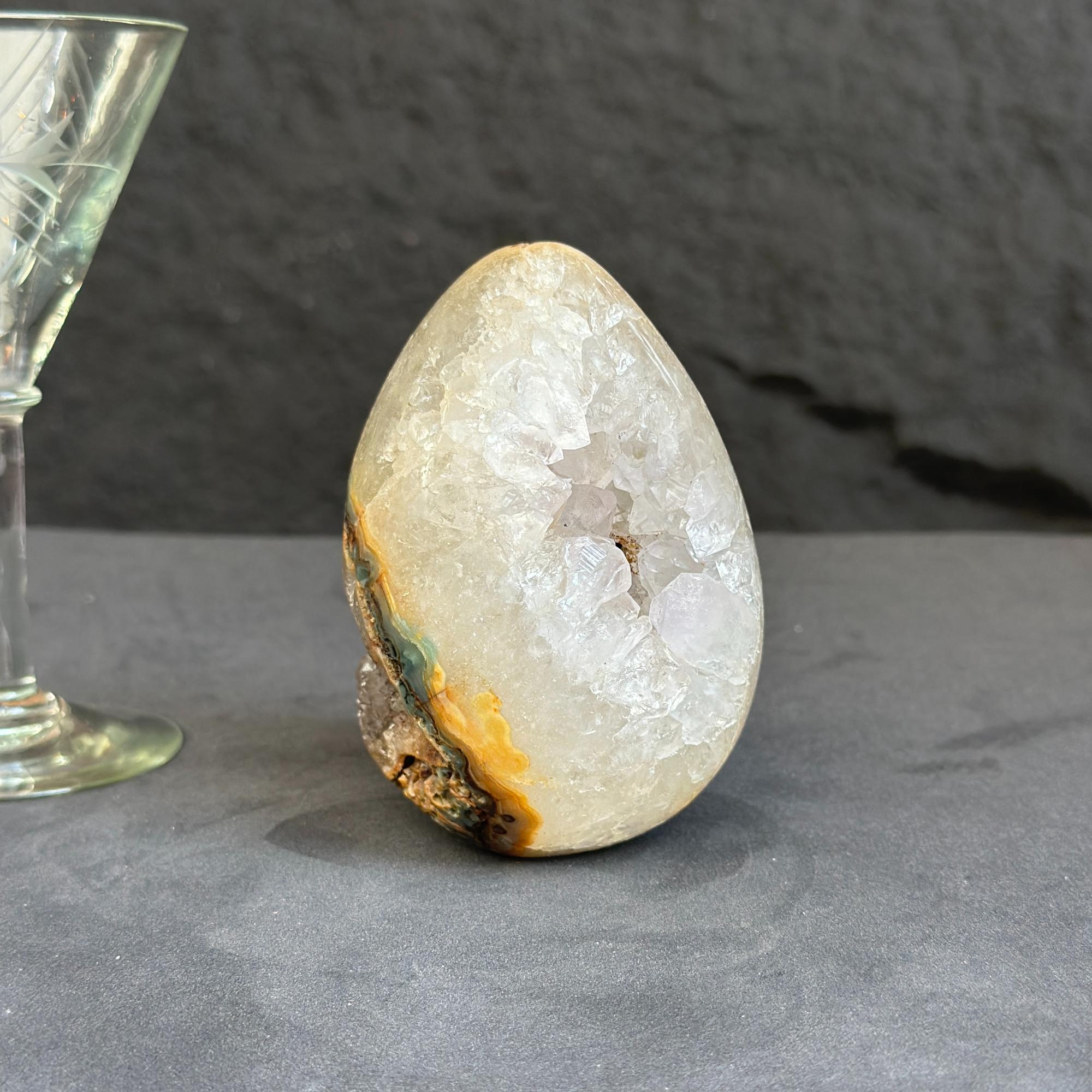 Geode crystal on a dark surface with a glass object in the background